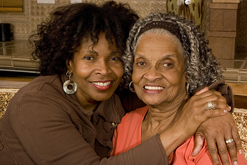 African american mother and daughter sitting closely on a couch smiling at the camera