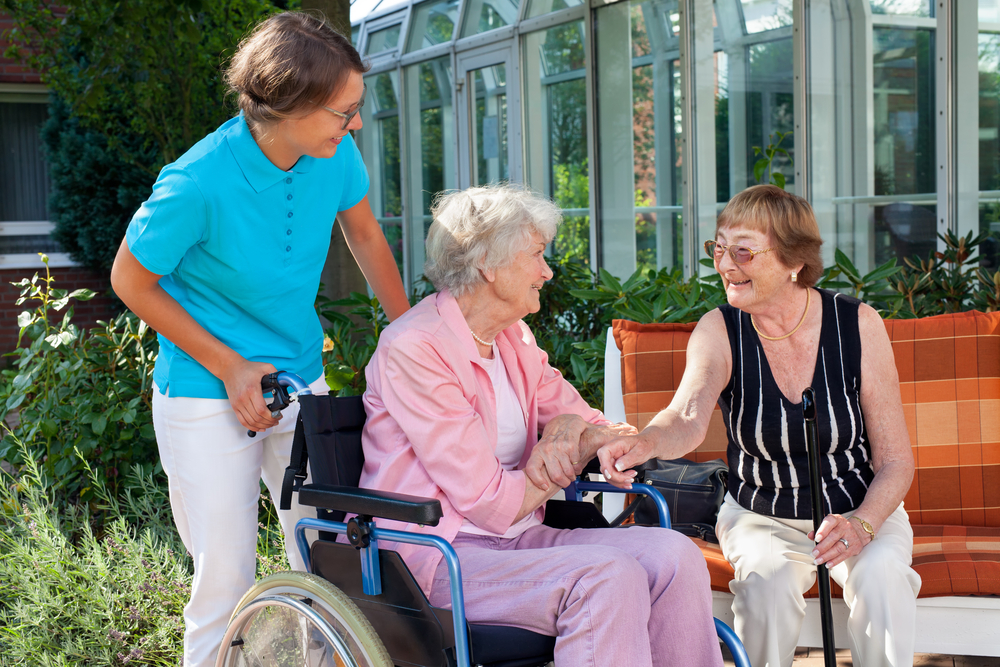 Photo of nurse with a patient in a wheelchair greeting a fellow patient who is sitting on a bench
